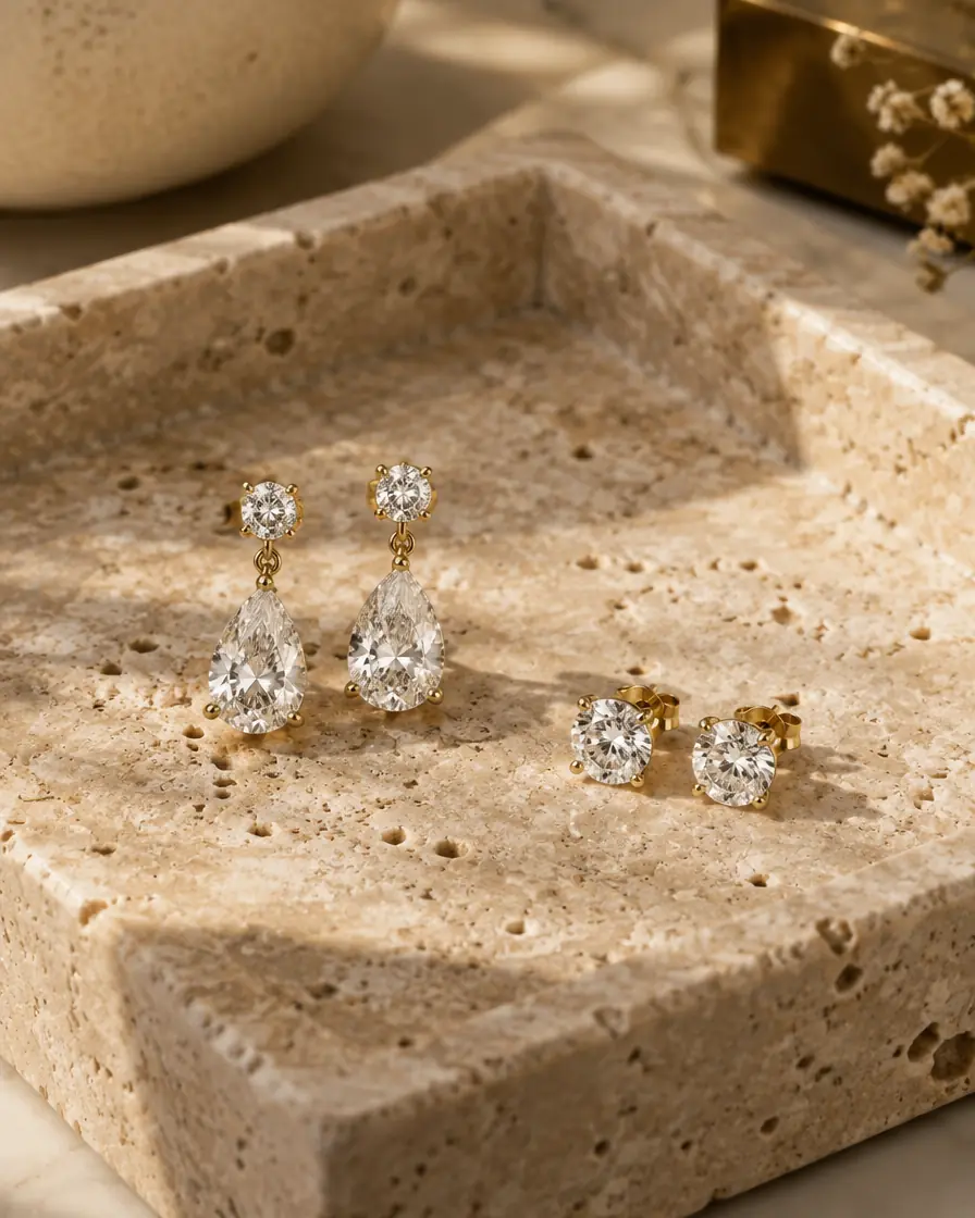 Diamond drop earrings and round diamond studs in yellow gold on a travertine tray